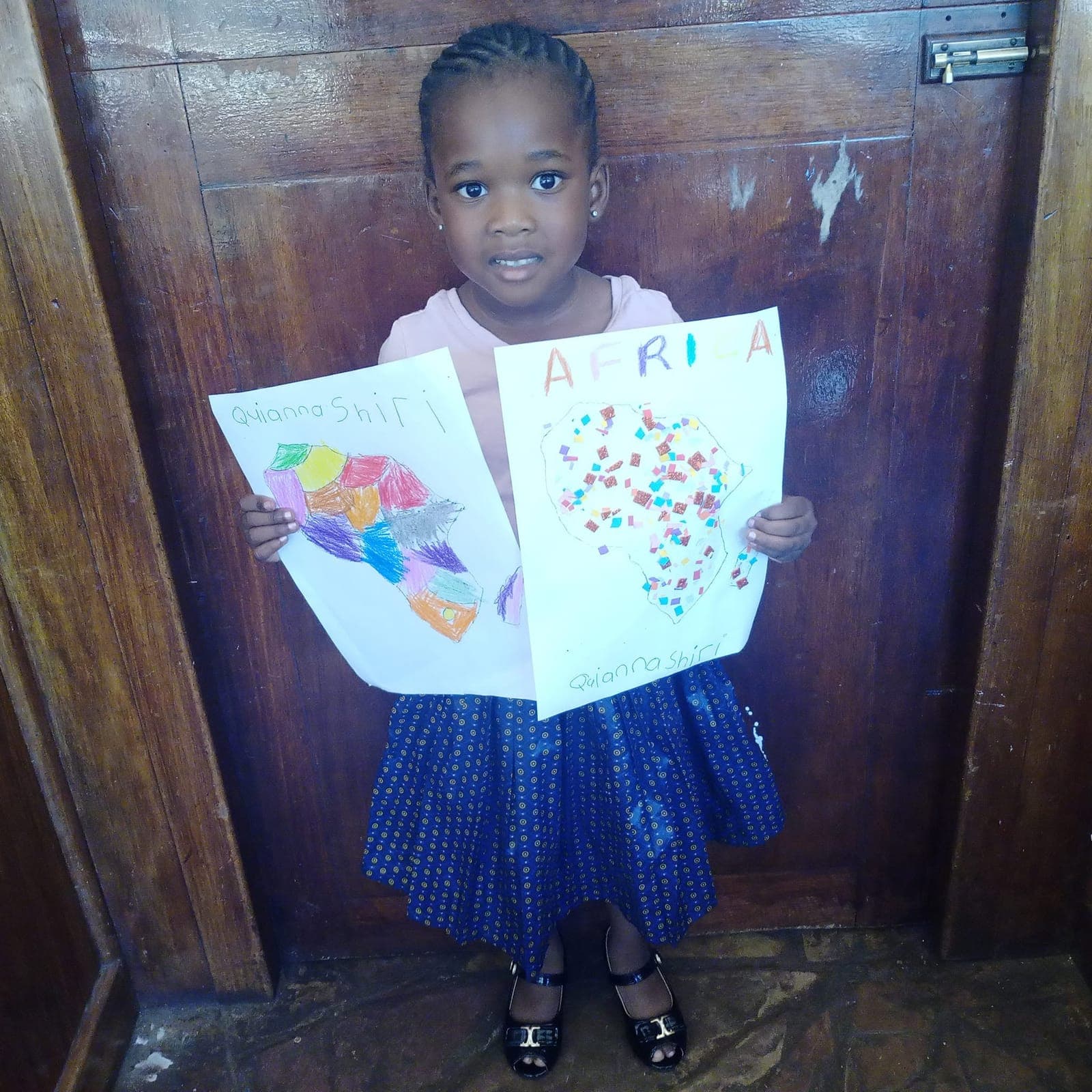 A child at Nirmeen holding up two pieces of artwork made in class