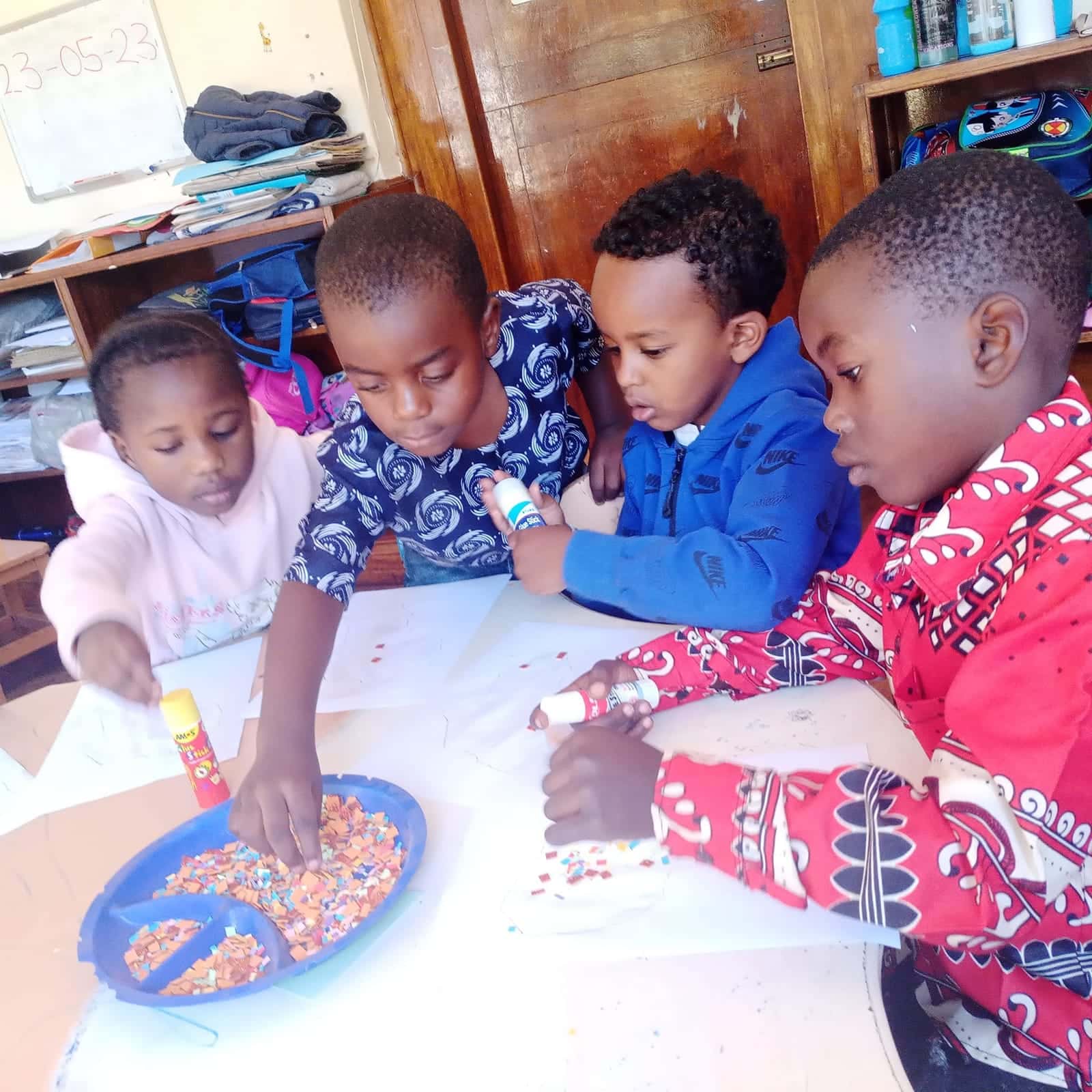 Four children making a collage with coloured paper at an art table at Nirmeen Nursery & Junior School, Belvedere