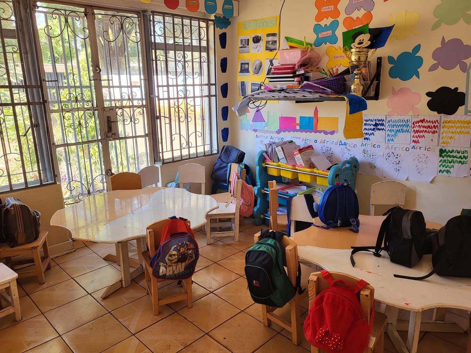 A bright classroom at Nirmeen with small tables and chairs, school bags and children's work on the walls