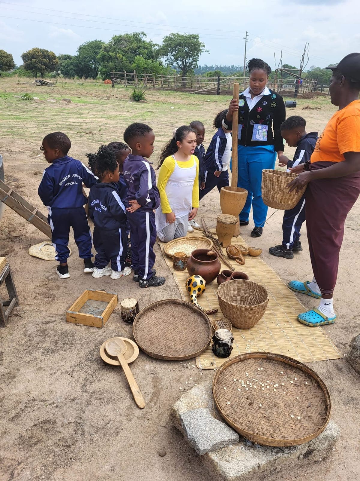 Children exploring woven baskets, clay pots and a wooden pestle and mortar on cultural day at Nirmeen