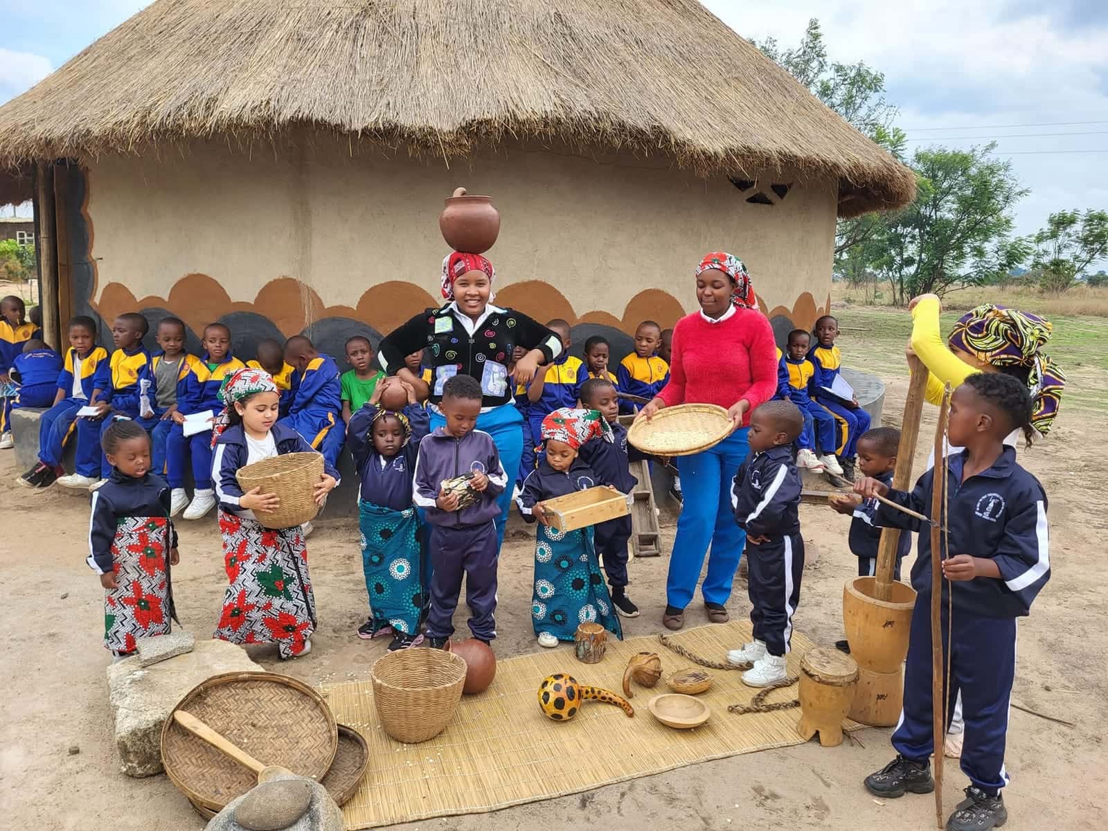 Children and teachers at a cultural day at Nirmeen, Belvedere, with clay pots, woven baskets and a thatched hut