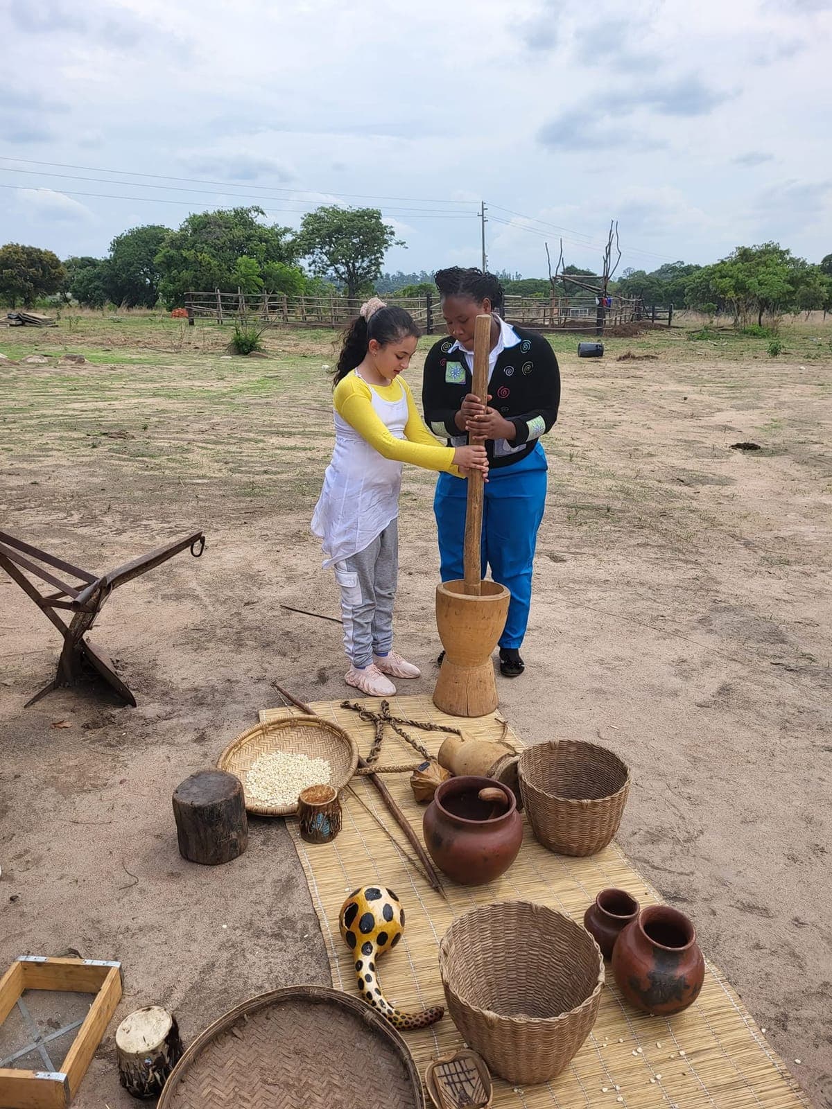 A child trying a traditional wooden pestle and mortar with a teacher on cultural day at Nirmeen