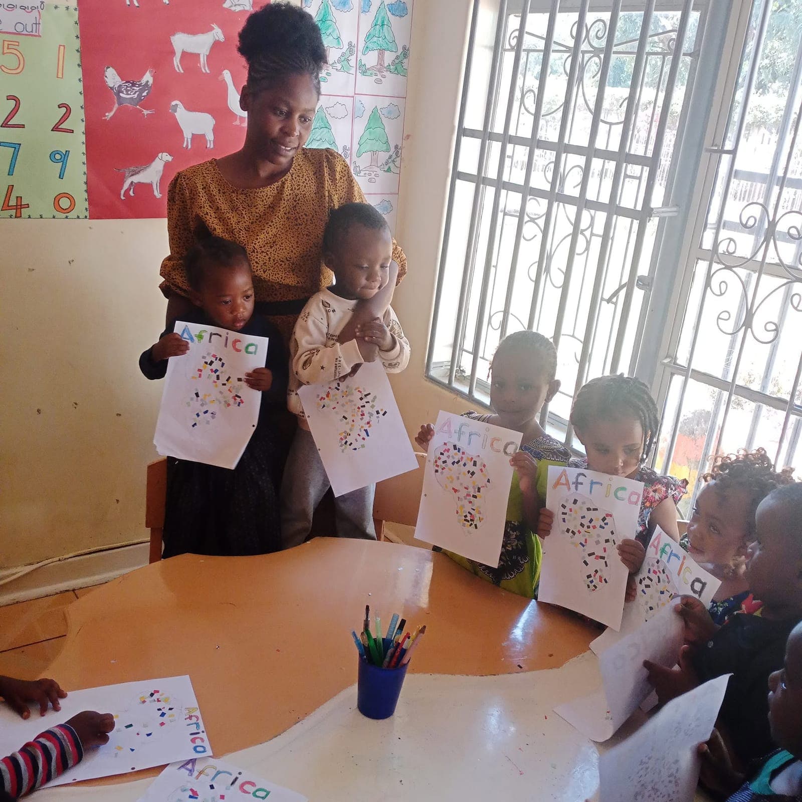 A teacher with children holding up their finished artwork in a classroom at Nirmeen, Belvedere